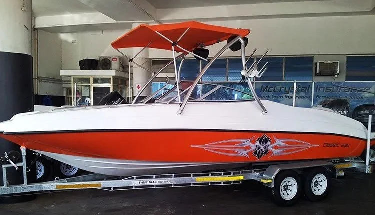 A classic orange and white speedboat on a trailer inside a garage or showroom.