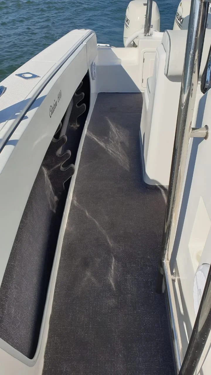 View of a boat deck with black textured flooring, white sides, and an outboard motor in the water.