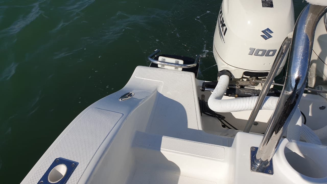 View of the back of a small boat with a Suzuki 100 outboard motor, white deck, and water around it.