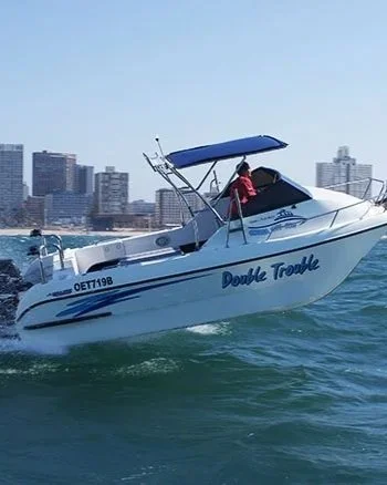 A white motorboat named 'Double Trouble' cruising on the water with a city skyline in the background.