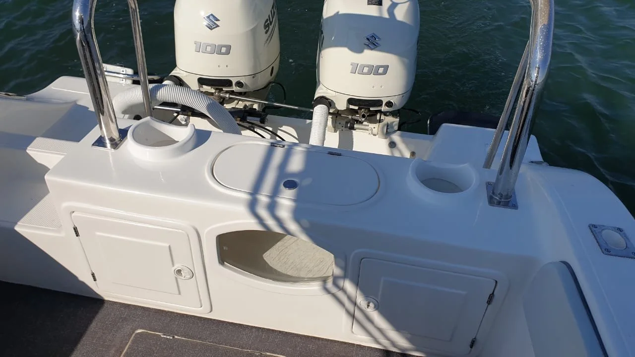 View of the back of a boat showing two Suzuki 100 horsepower outboard motors, with a white deck featuring built-in compartments and railings.