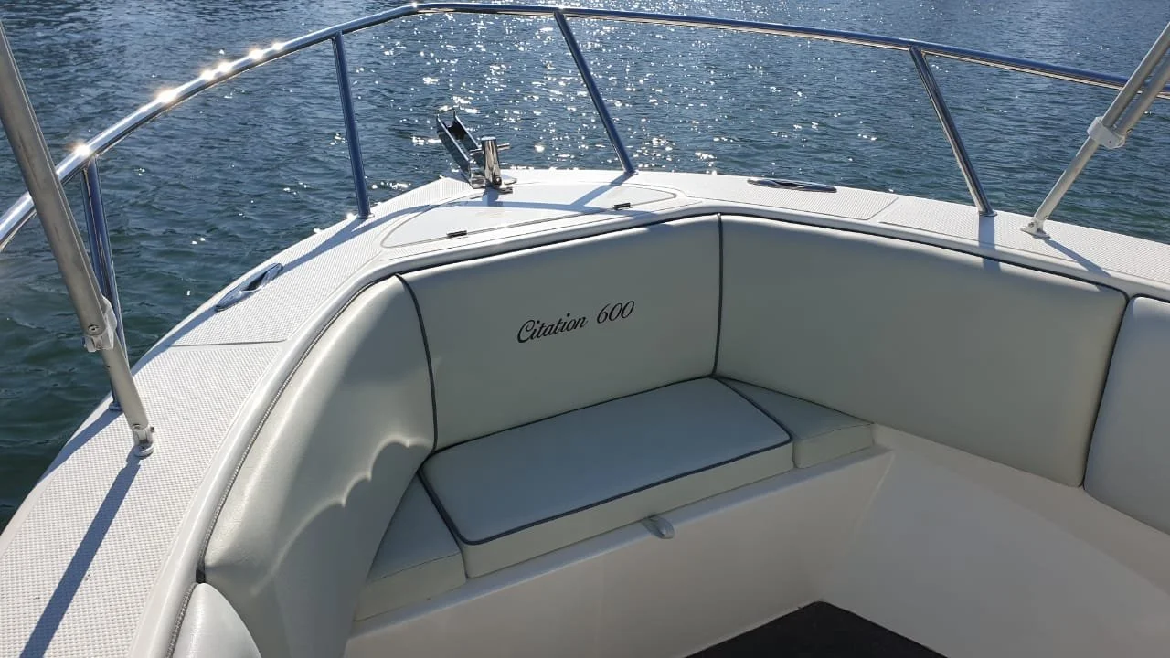 Close-up of a yacht's bow seating area with white cushions, stainless steel railing, and water in the background.
