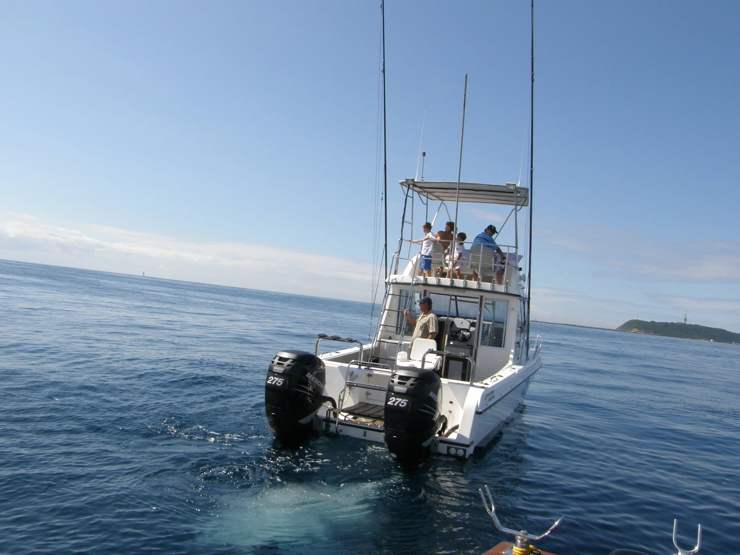 A boat with five people on a calm ocean under a clear blue sky, with land visible in the distance.