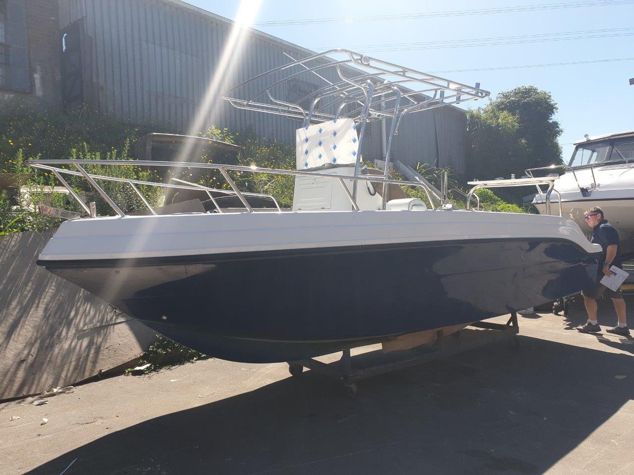 A boat on a trailer displayed outdoors, with a man standing nearby holding a pamphlet, and another boat in the background.