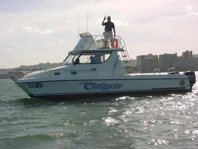 Man standing on boat named 'Eclipse' sailing in water near city skyline