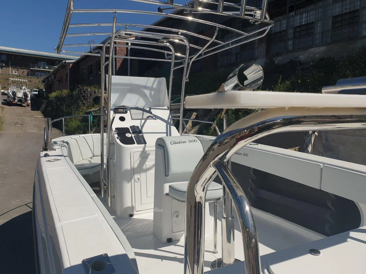 White Citation 600 boat with metal frame and seating docked on land near buildings under a blue sky.