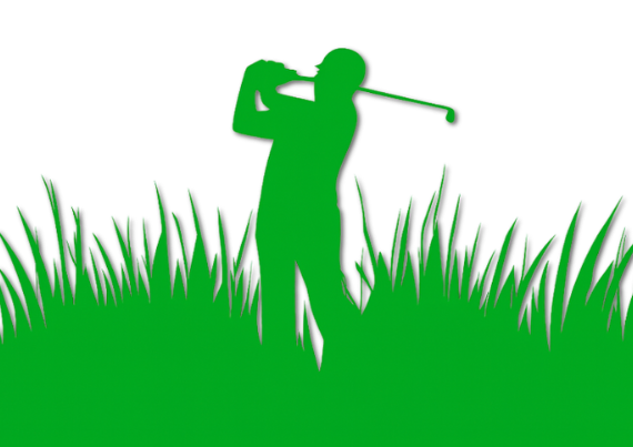 Silhouette of a golfer in a green field swinging a golf club.
