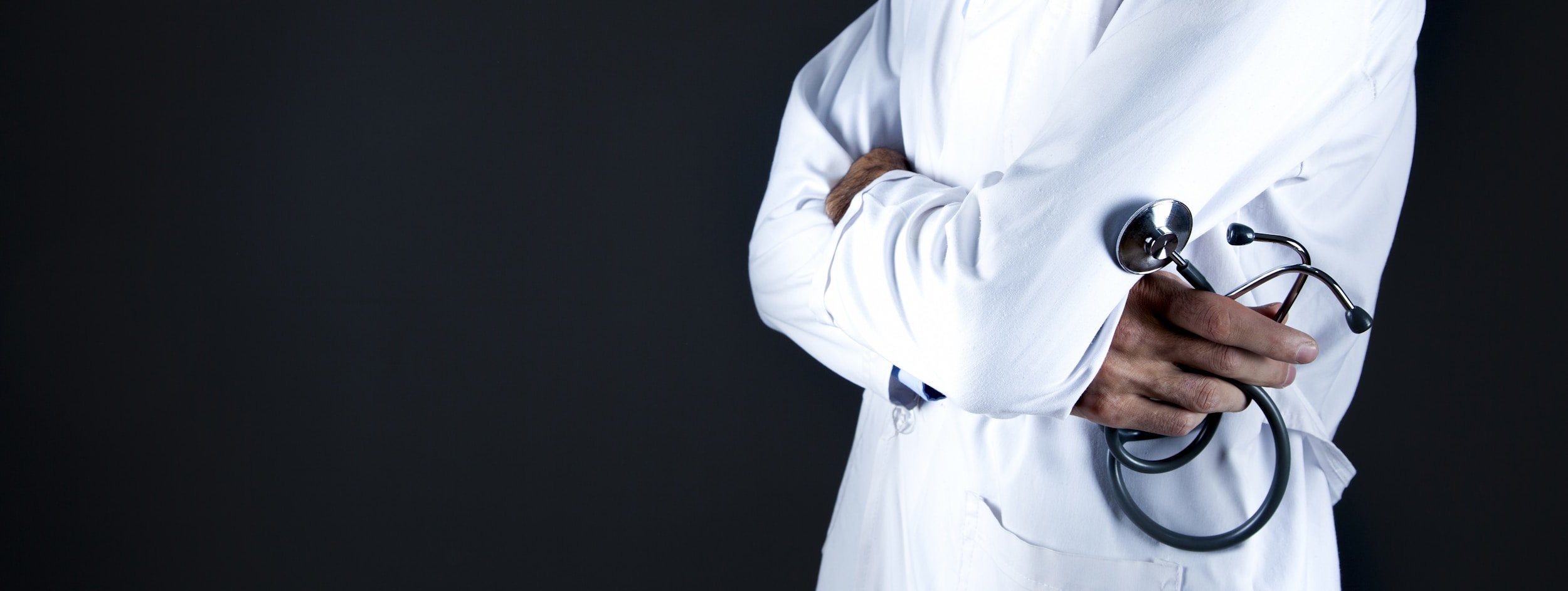 Doctor con bata blanca y estetoscopio en brazos cruzados.