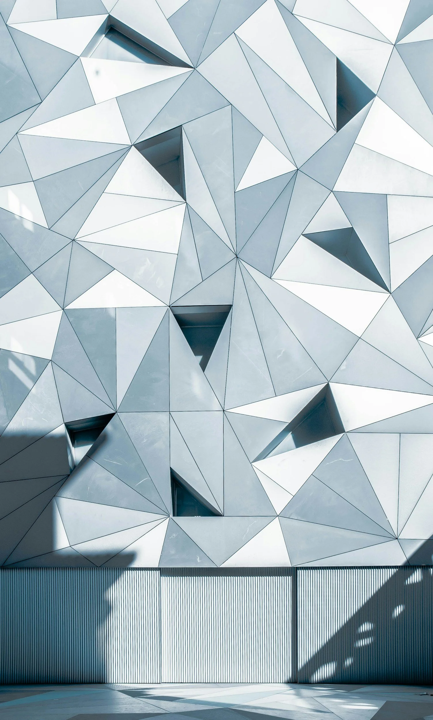 Close-up of a modern building's facade with geometric, triangular metal panels and shadowed areas.