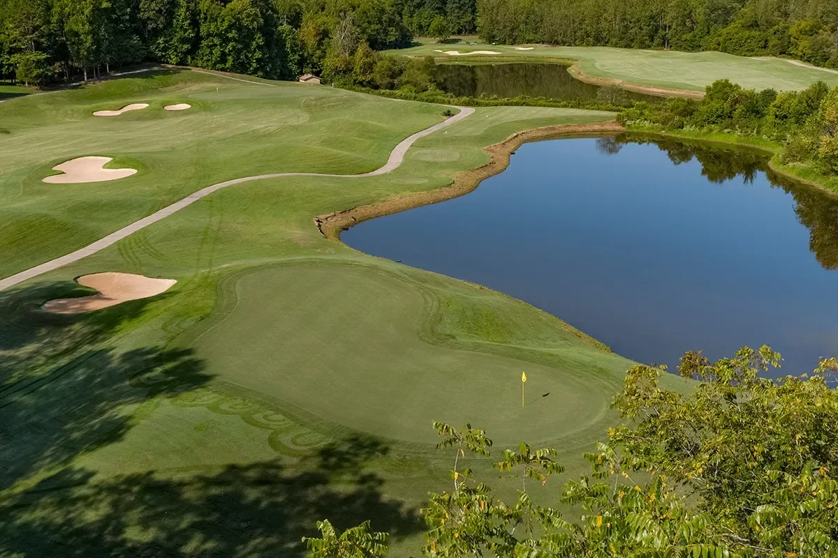 A scenic golf course with a putting green, sand bunkers, water hazard, and trees surrounding the area.