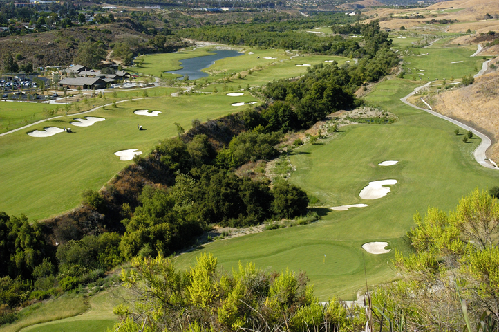 Aerial view of a golf course with multiple holes, sand traps, and greens, surrounded by trees and rolling hills.
