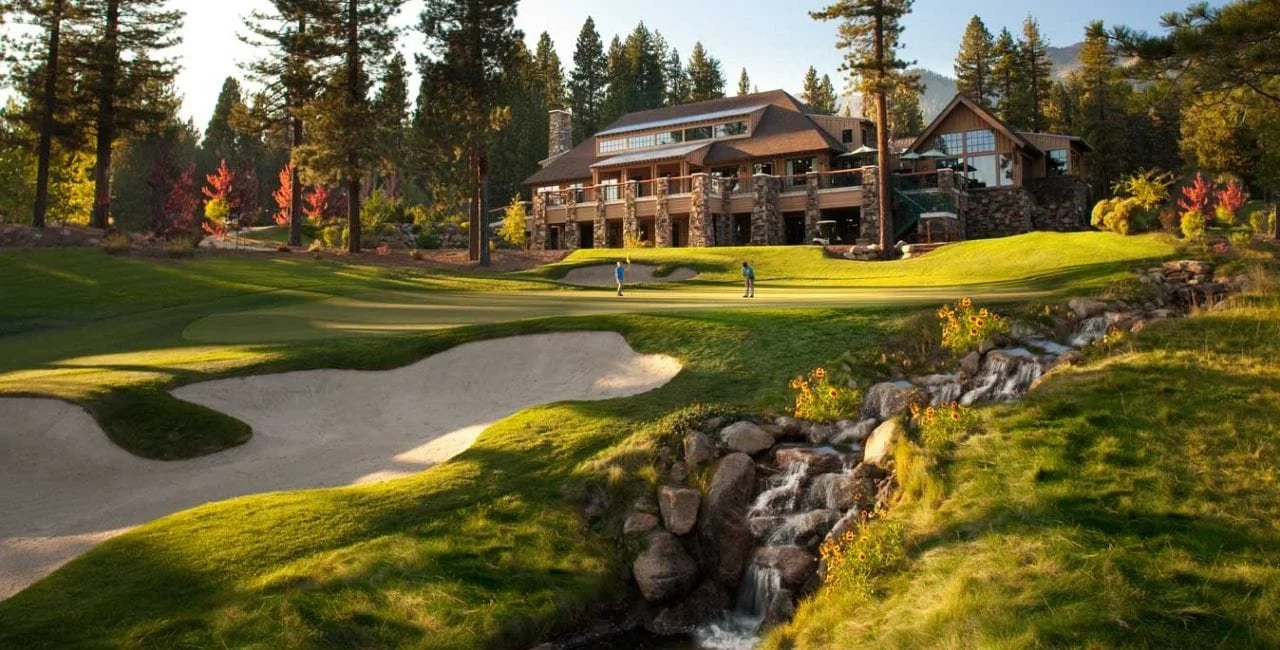 A luxurious house overlooking a golf course with two golfers playing, surrounded by trees and a small stream.