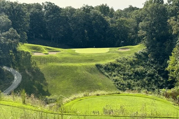A golf course with green fairways, sand bunkers, and trees surrounding the area.