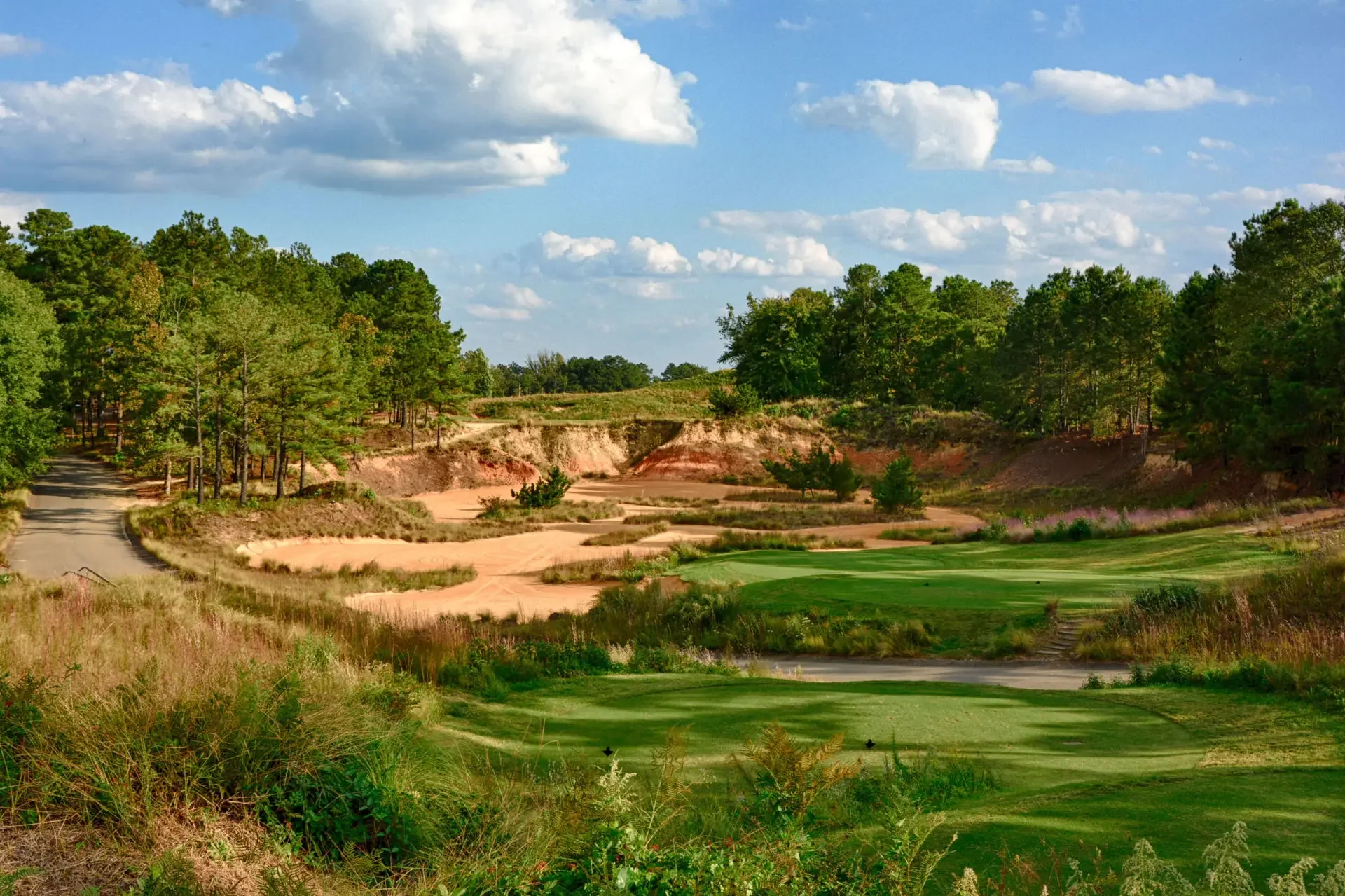 A scenic view of a golf course surrounded by trees and hills, with a partly cloudy sky overhead.