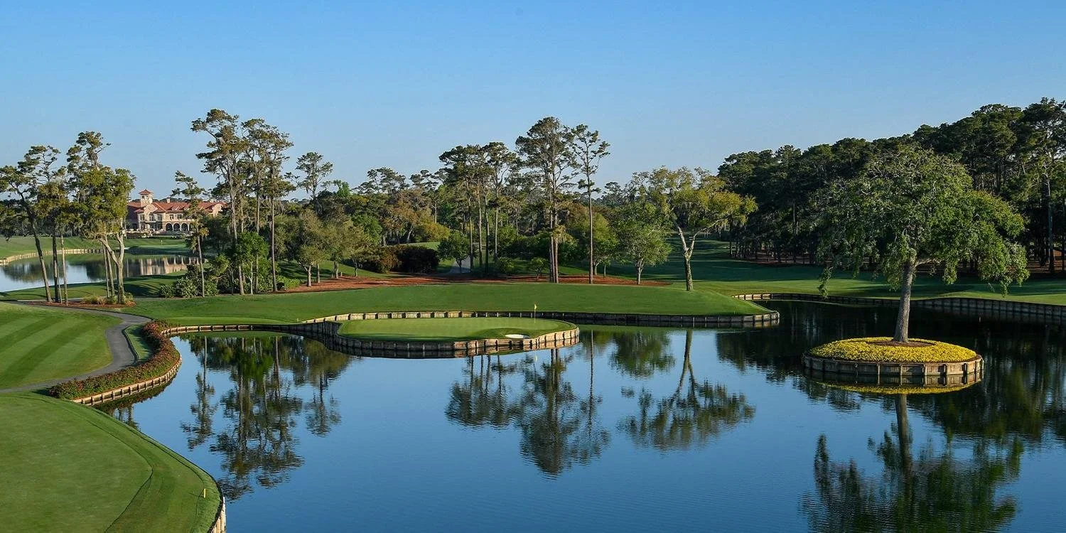 Scenic golf course with water hazards, trees, and a clubhouse in the background.