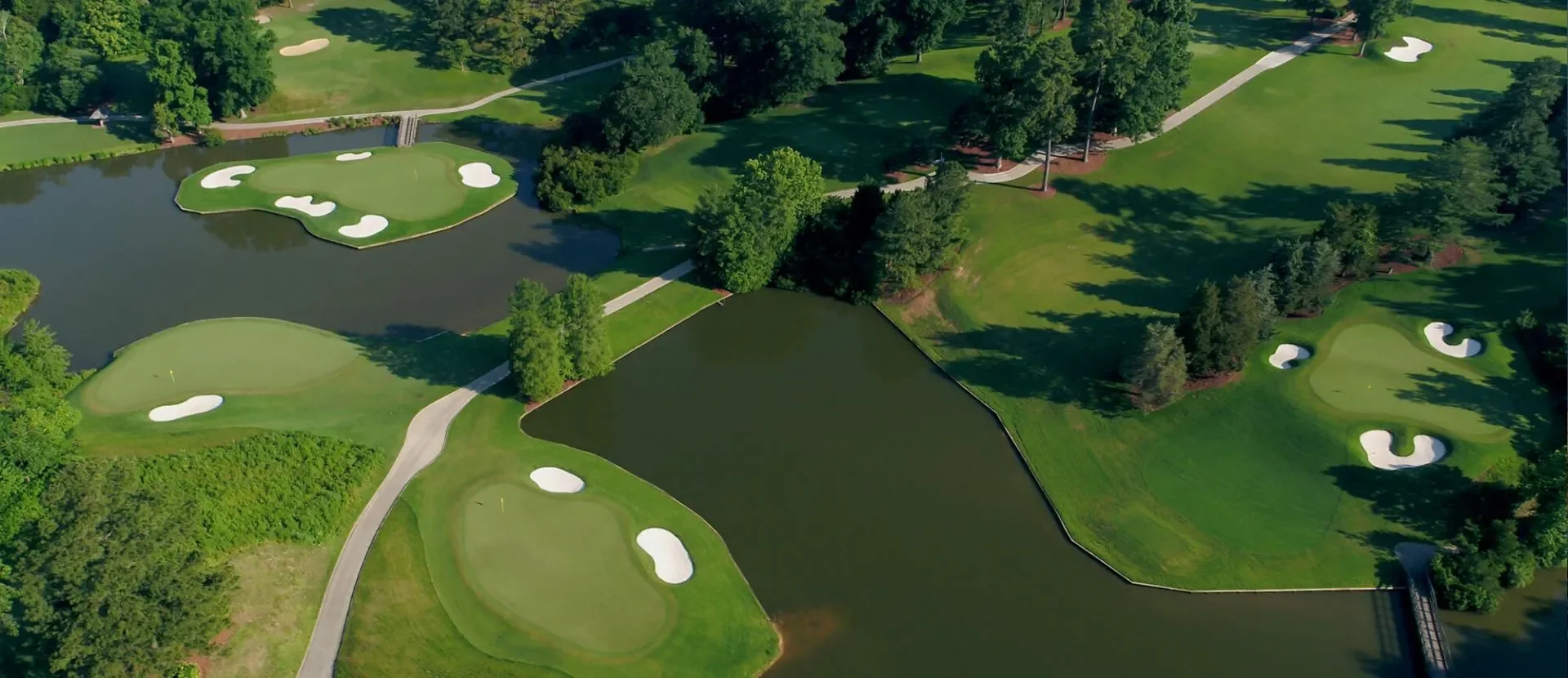Aerial view of a golf course with multiple holes, sand bunkers, water hazards, green fairways, and trees.