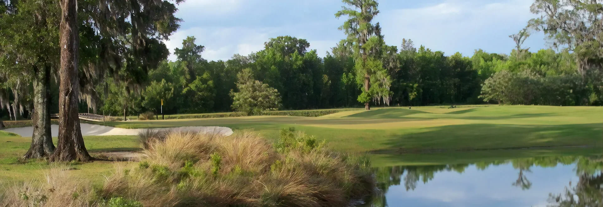 A scenic golf course with lush green fairways, trees, a water hazard, and a flag marking the hole, set against a background of dense forest.