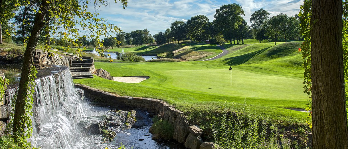 A scenic golf course with a water feature, trees, and a well-maintained putting green.