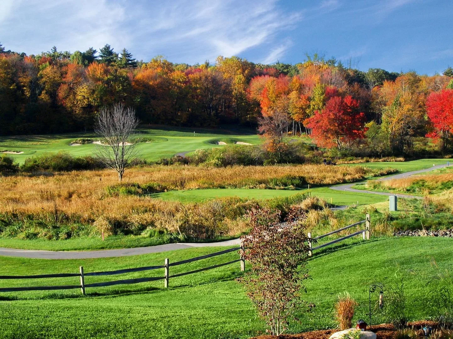 A scenic golf course surrounded by trees with autumn foliage, green grass, and a clear blue sky.