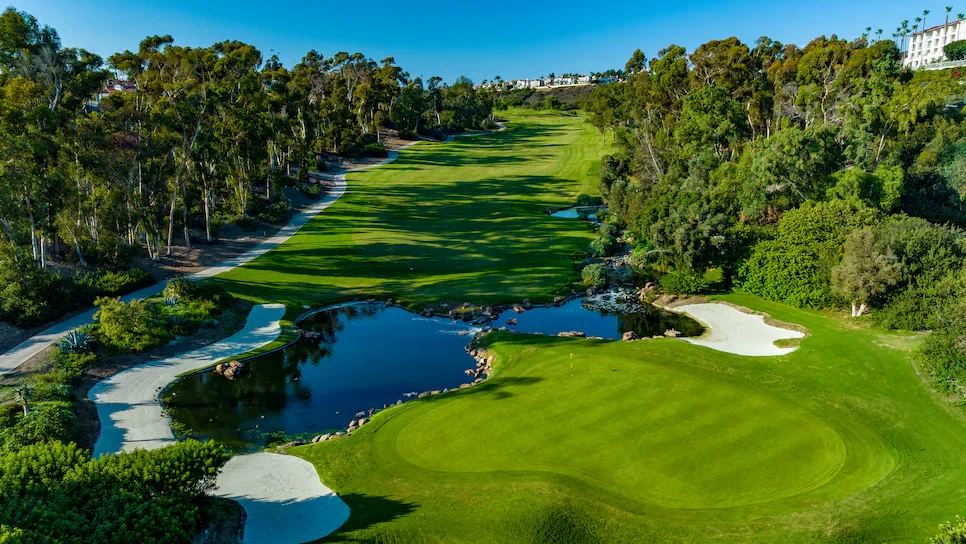Aerial view of a golf course with green fairways, sand traps, and water hazards surrounded by trees and shrubbery.