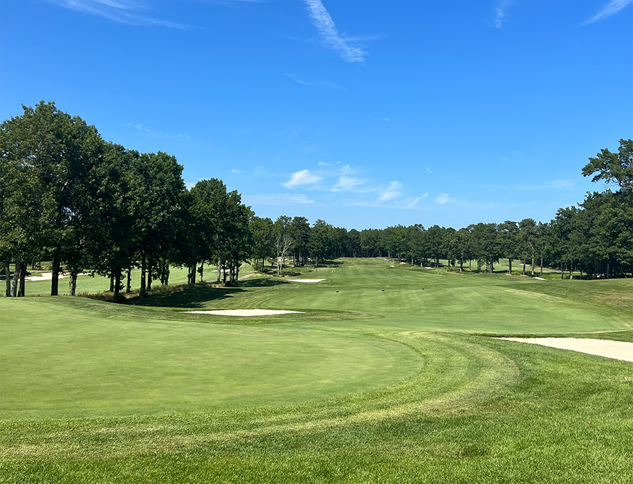 A clear view of a golf course with a green, sand bunkers, and trees under a bright blue sky.