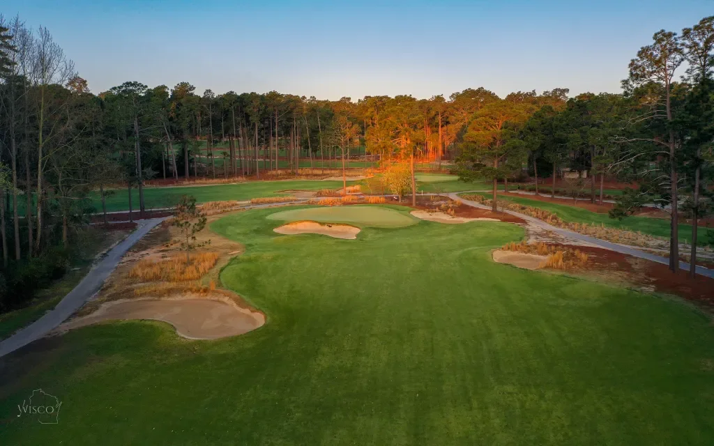 A golf course fairway with sand bunkers, surrounded by trees at sunset.