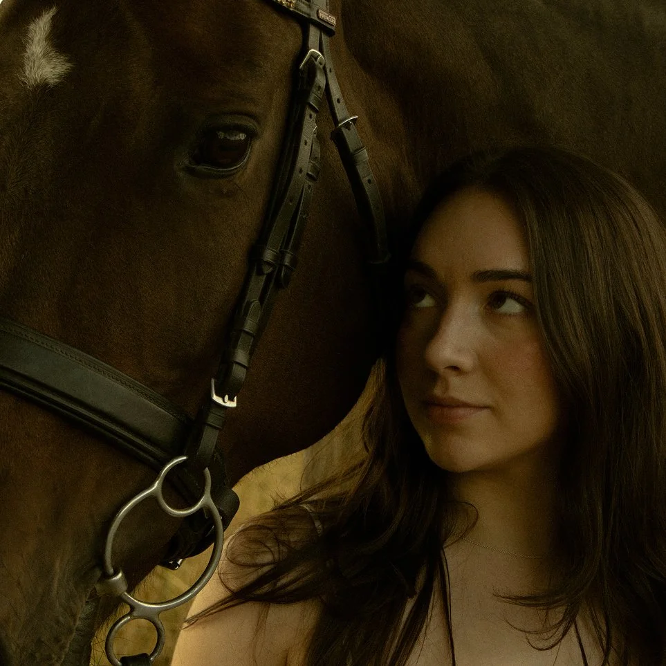 Woman standing beside a horse in a sunlit field, framed through a cinematic lens by Sela Volk.