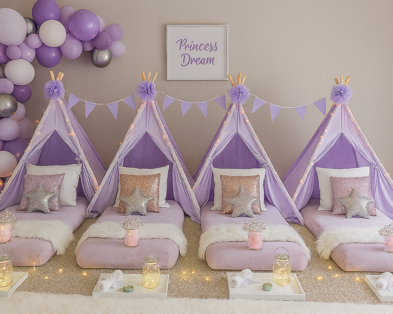 A children's princess-themed sleepover setup with four purple tents decorated with fairy lights and pom-poms, each bed with a pink sequin star pillow, a fuzzy blanket, and small jars with lights, with purple and silver balloons and a framed sign that says 'Princess Dream' in the background.