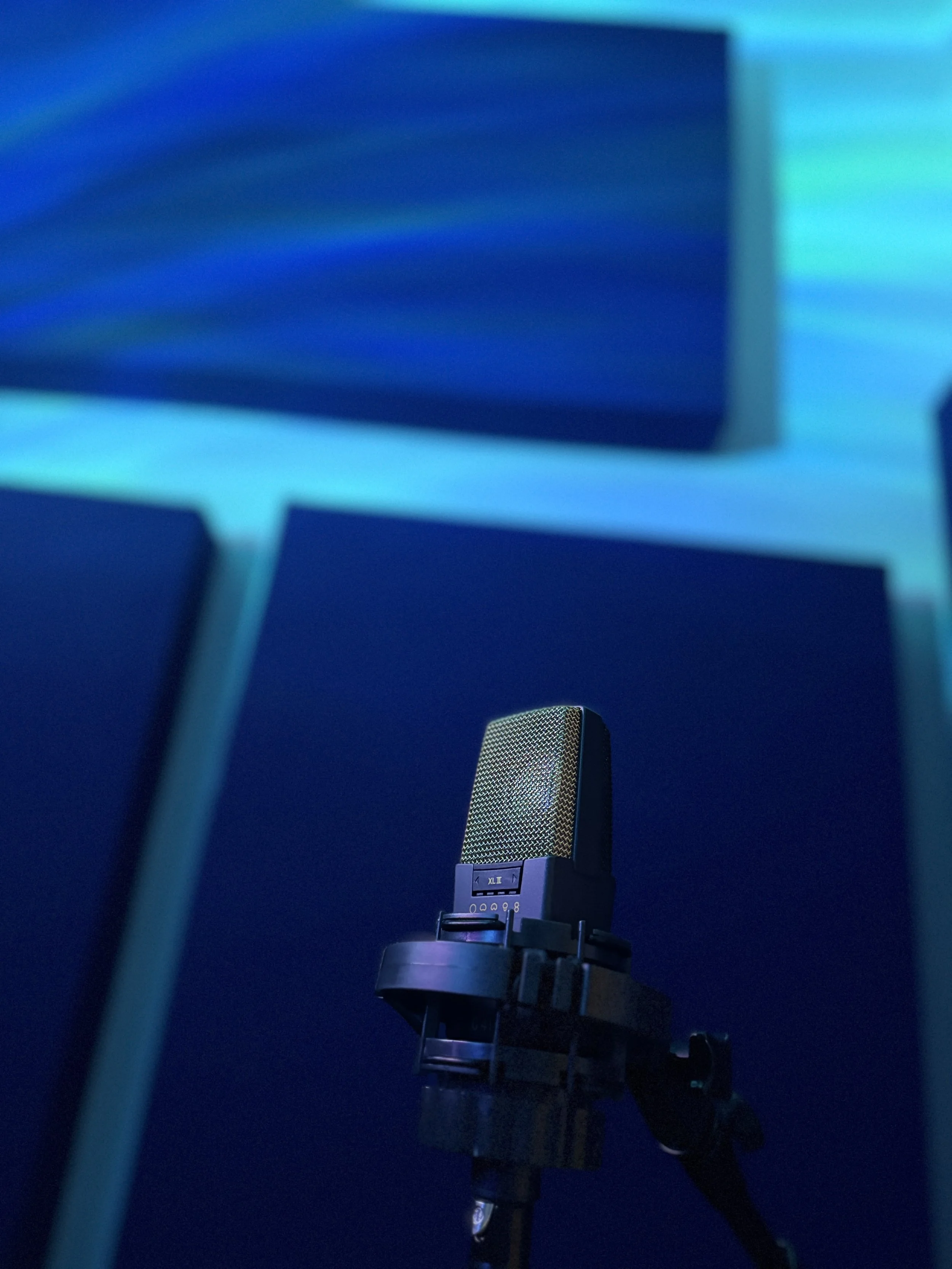 A AKG C414 studio microphone on a stand in a room with blue and teal lighting.