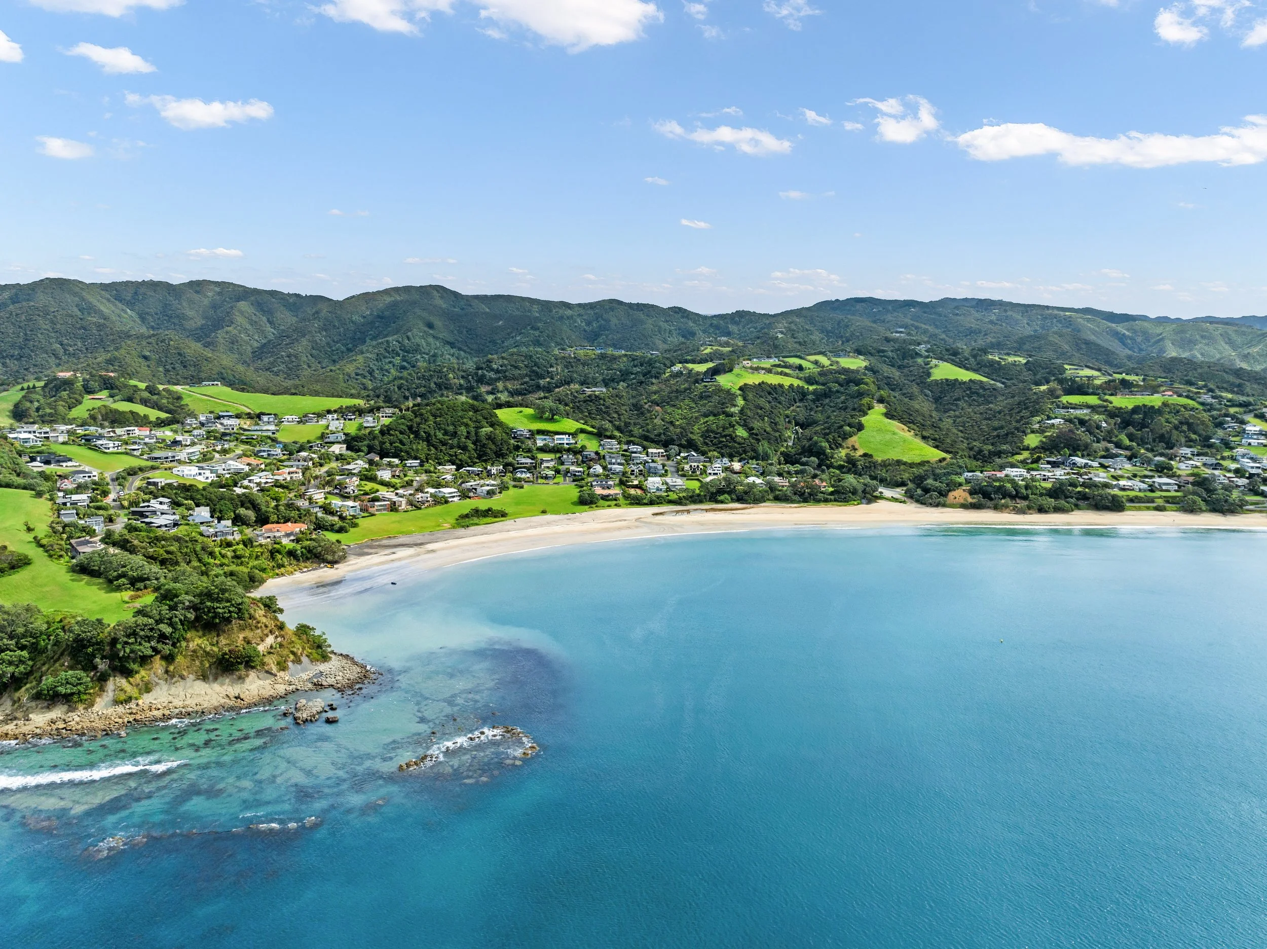 Beautiful aerial drone view of Langs Beach coastal properties and turquoise waters, showcasing the premium Northland lifestyle. Sell your Bream Bay property with James Alexander and Charlotte Daun.