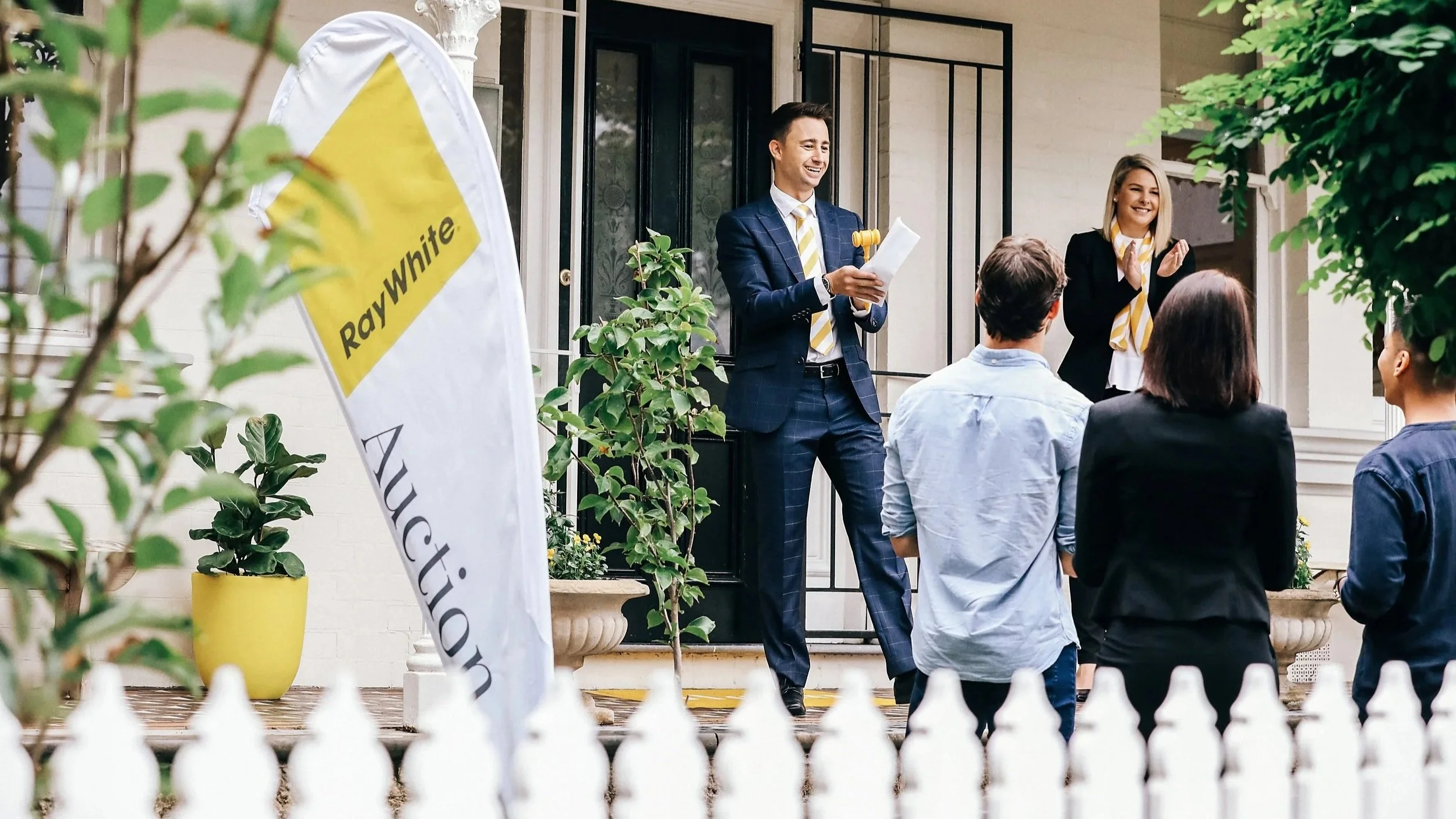 Ray White real estate auctioneer holding a gavel at a live property auction in Bream Bay. Top area agents James Alexander and Charlotte Daun