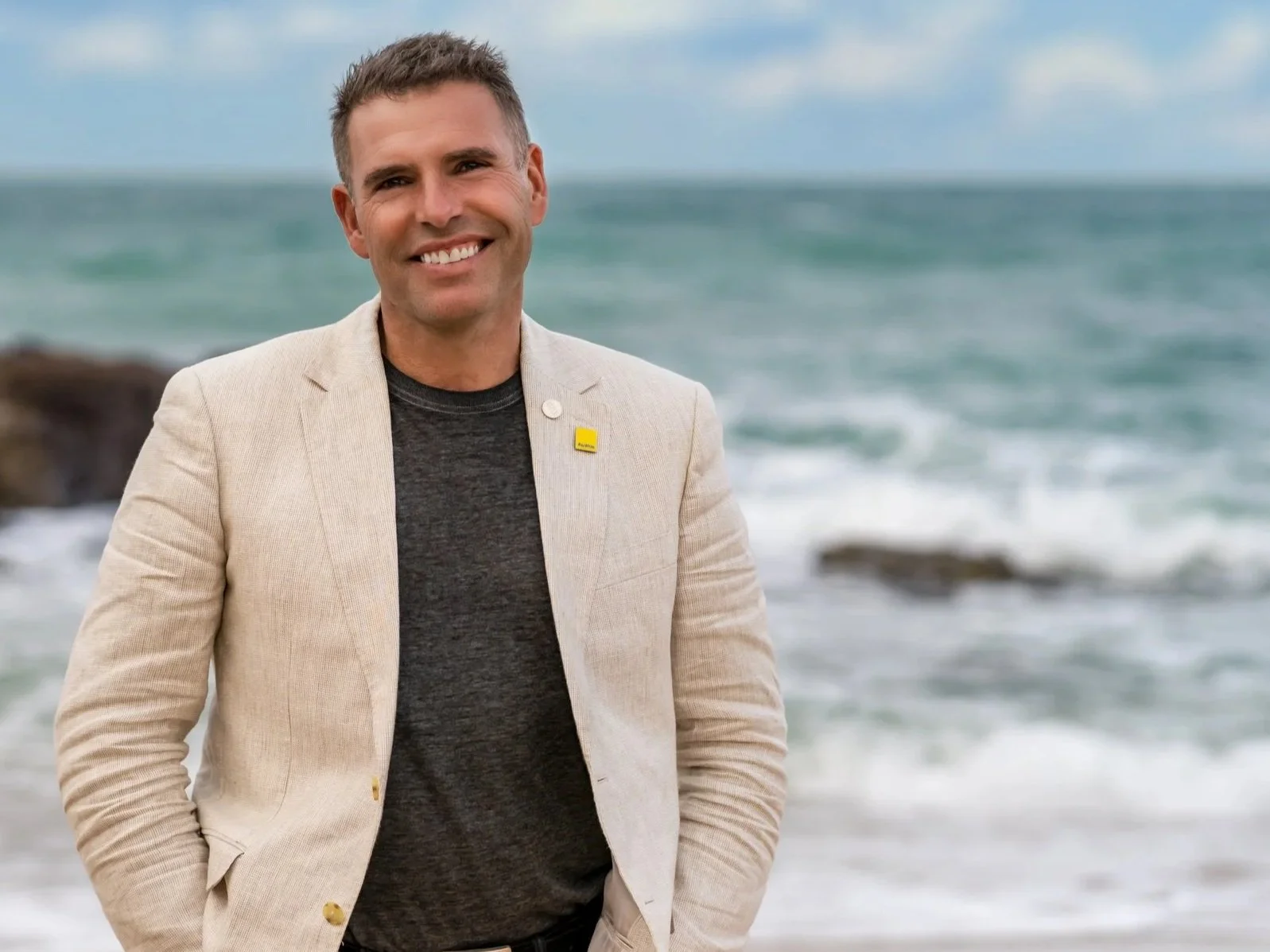Bream Bay real estate agent James Alexander smiling on a local Langs Beach, wearing a beige blazer.