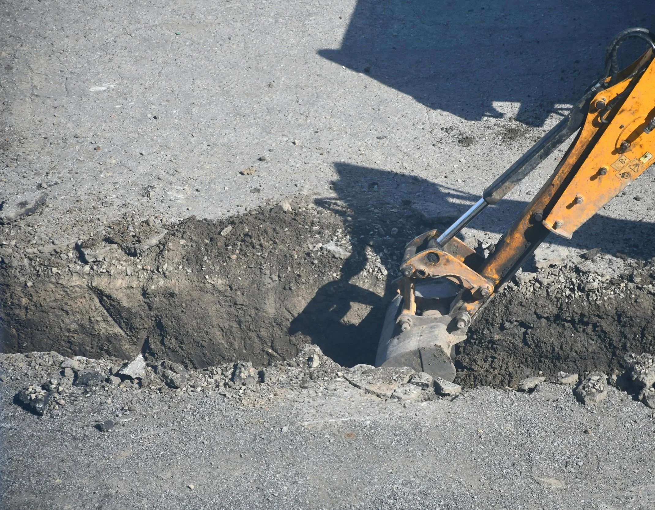 Close-up of a yellow mini excavator digging a trench in a gravel road.