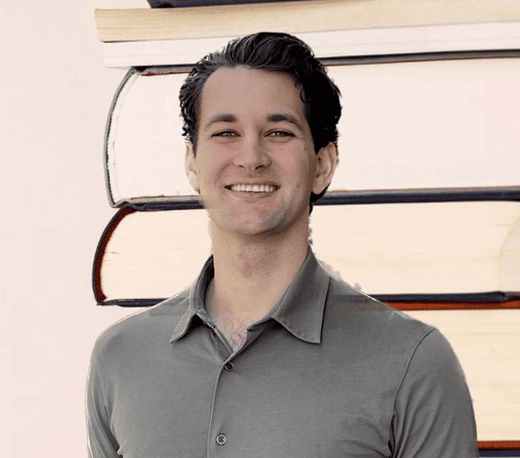 A man smiling in front of a background with stacked books.