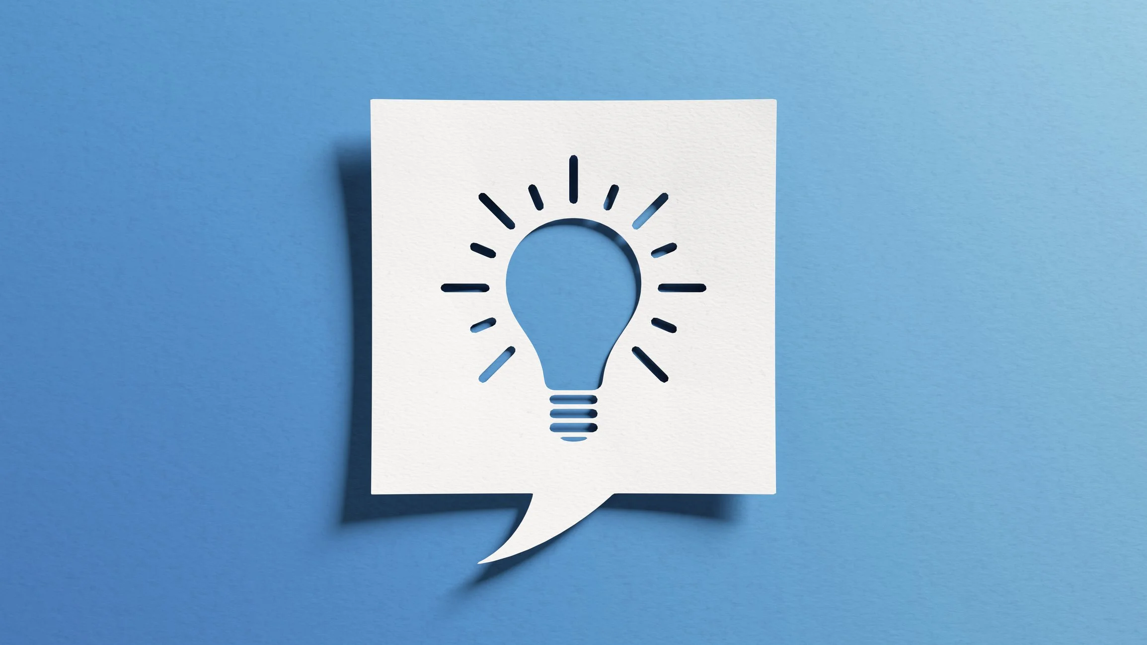 A white paper cutout of a speech bubble with a lightbulb icon, placed on a blue background, symbolizing an idea or innovation.