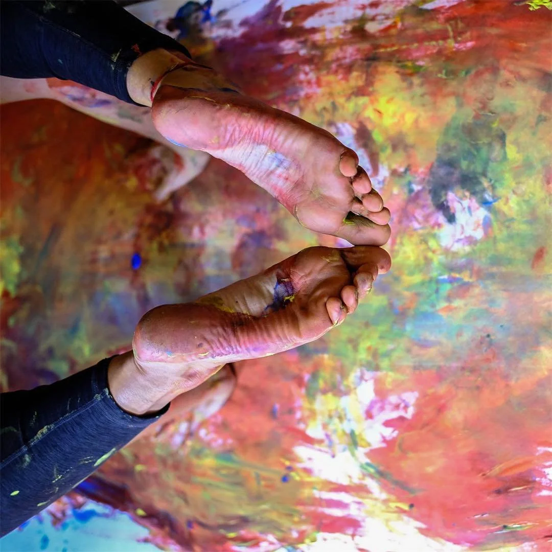 Füße, die mit bunten Farben auf einer künstlerischen, getrockneten Oberfläche eine Yogapose machen.