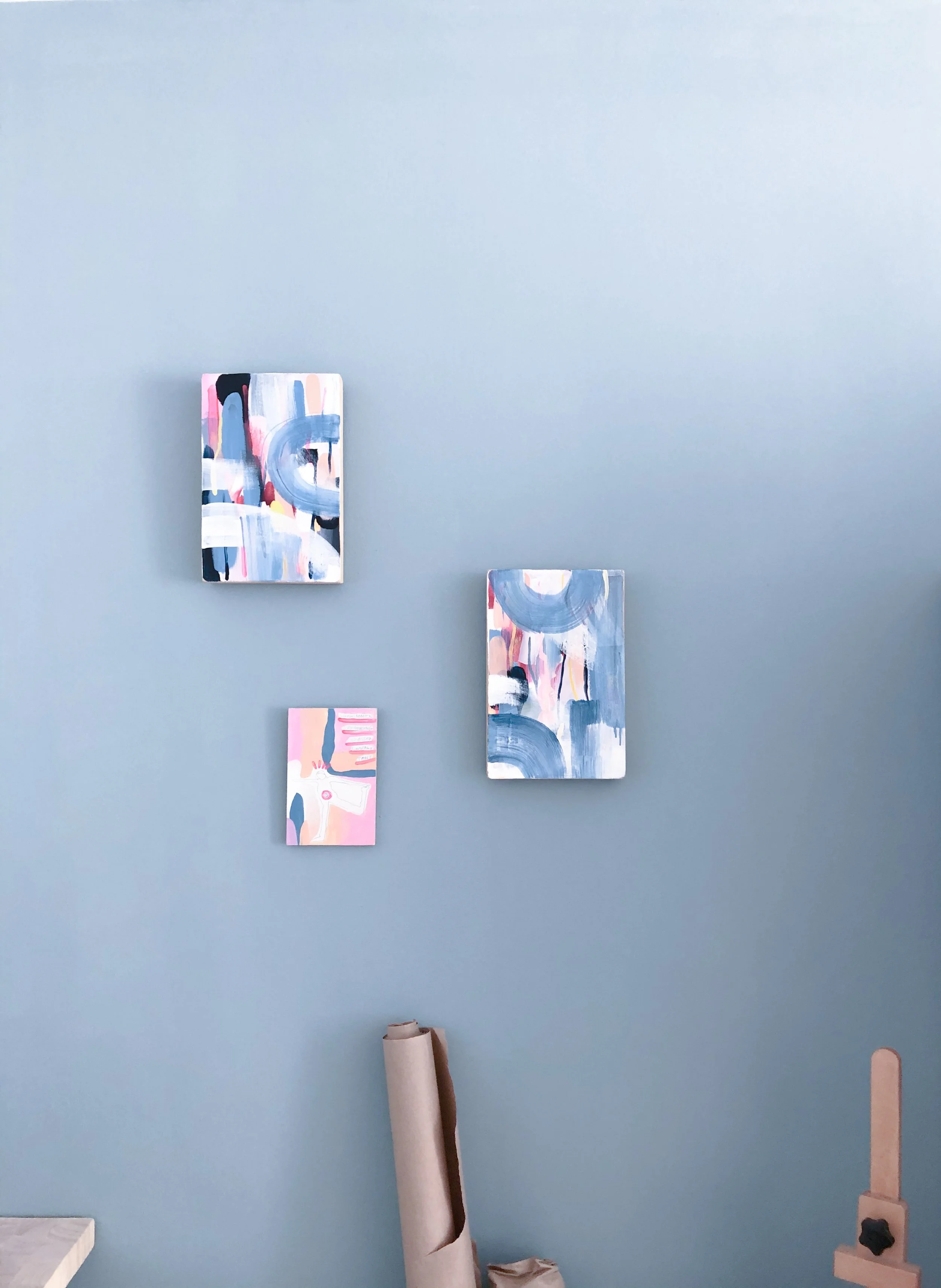 Drei abstrakte Gemälde in pastelfarben auf einer blauen Wand.