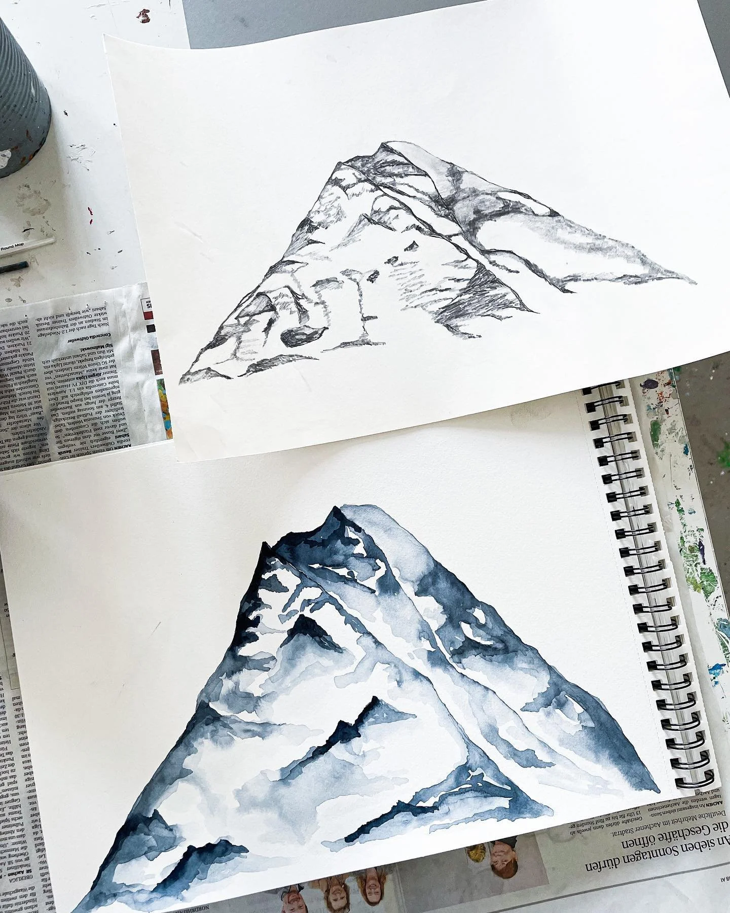 Zwei Skizzen von Bergen, eine in Bleistiftzeichnung und eine in Aquarell, auf weißen Papieren. Das obere Bild zeigt eine einfache, dunkle Skizze eines Berges, das untere Bild eine detaillierte, farbige Darstellung eines Bergs in Blau- und Grautönen.