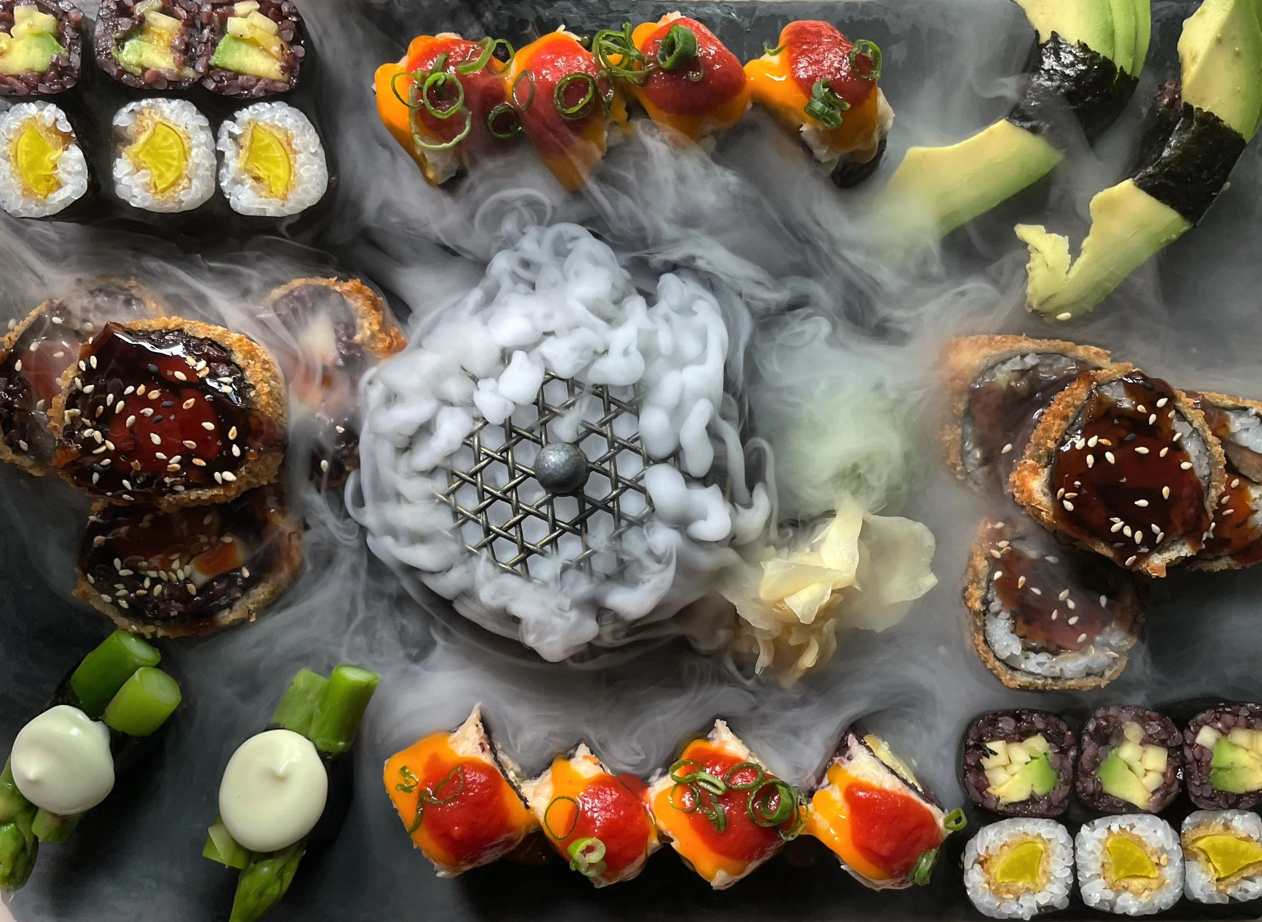 Verschiedene Sushi-Rollen mit rotem, grünem, gelbem und schwarzem Fisch, Avocado, Gurke und Sauce, auf einem dunklen Teller