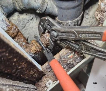 Plumber using a pipe wrench and pliers to repair or remove a rusted pipe in a plumbing system.