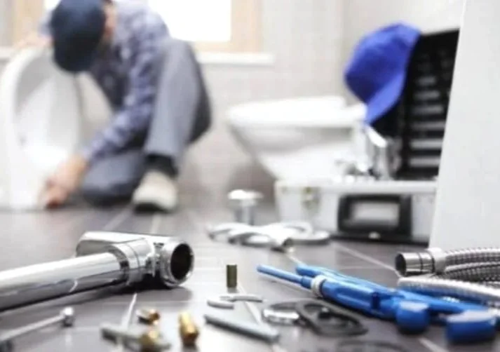 A person working on a plumbing project with various plumbing tools and pipes on a countertop in a bathroom.