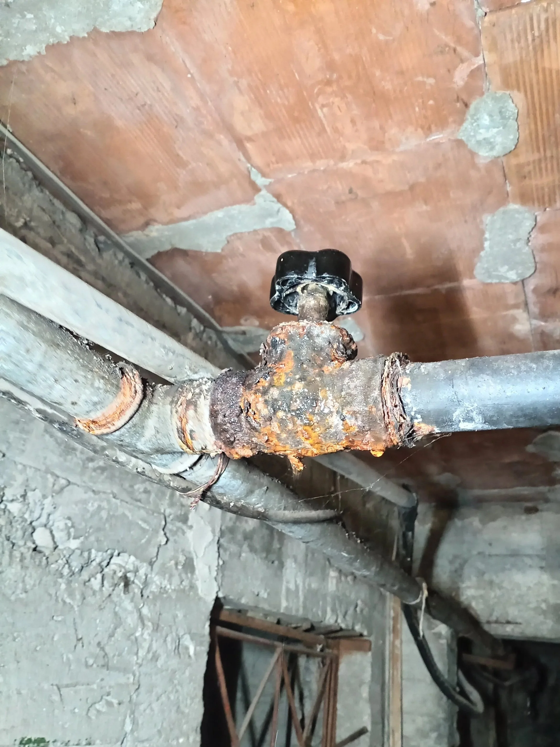 Corroded and rusty water pipe with a valve in an unfinished basement or utility room.