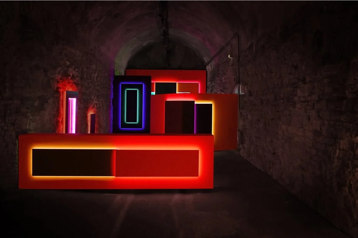 Colorful neon art installation with rectangular frames and glowing lights in a dark brick tunnel.