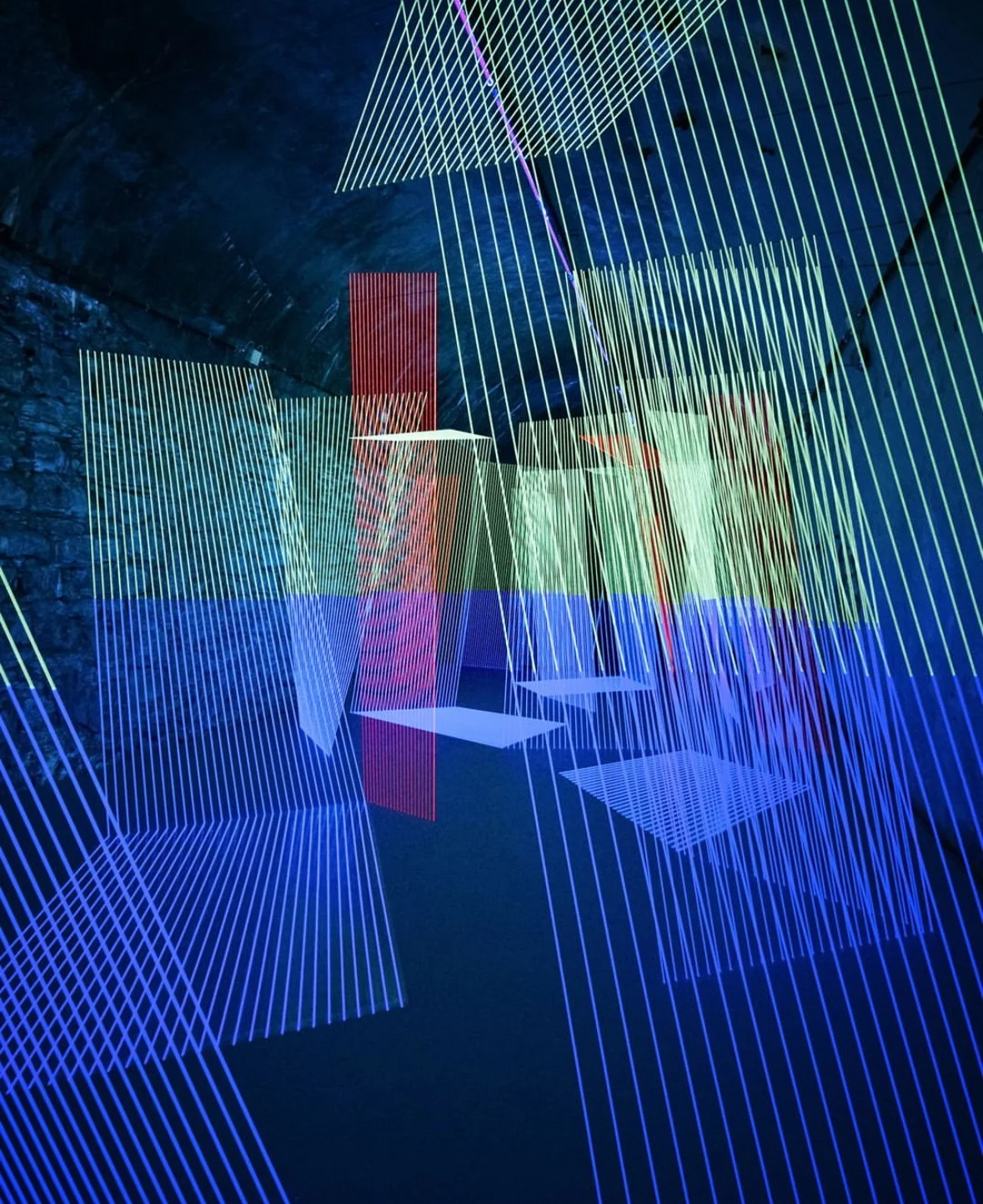 Installation art with colorful neon light lines and geometric shapes in a dark room.