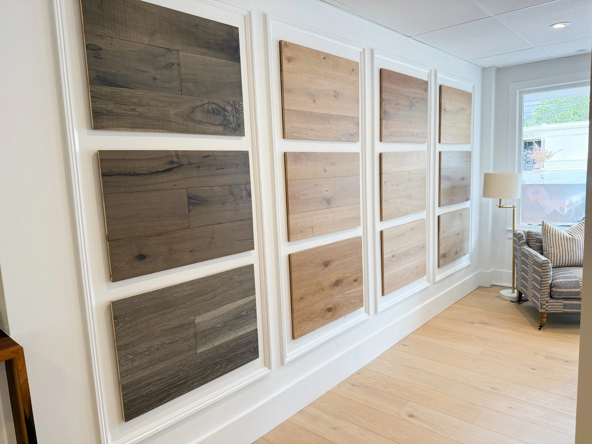 South Shore hardwood flooring samples displayed on a white wall in the Doyle Wood Flooring showroom, with a sofa and floor lamp near a bright window.