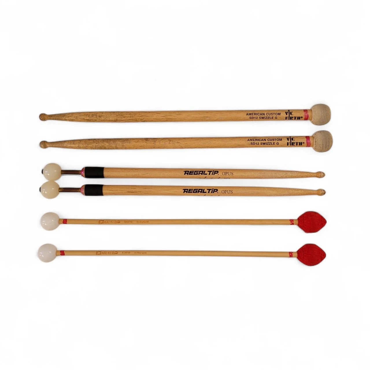 Six drumsticks, three with rounded heads and three with red tips, arranged horizontally against a white background.