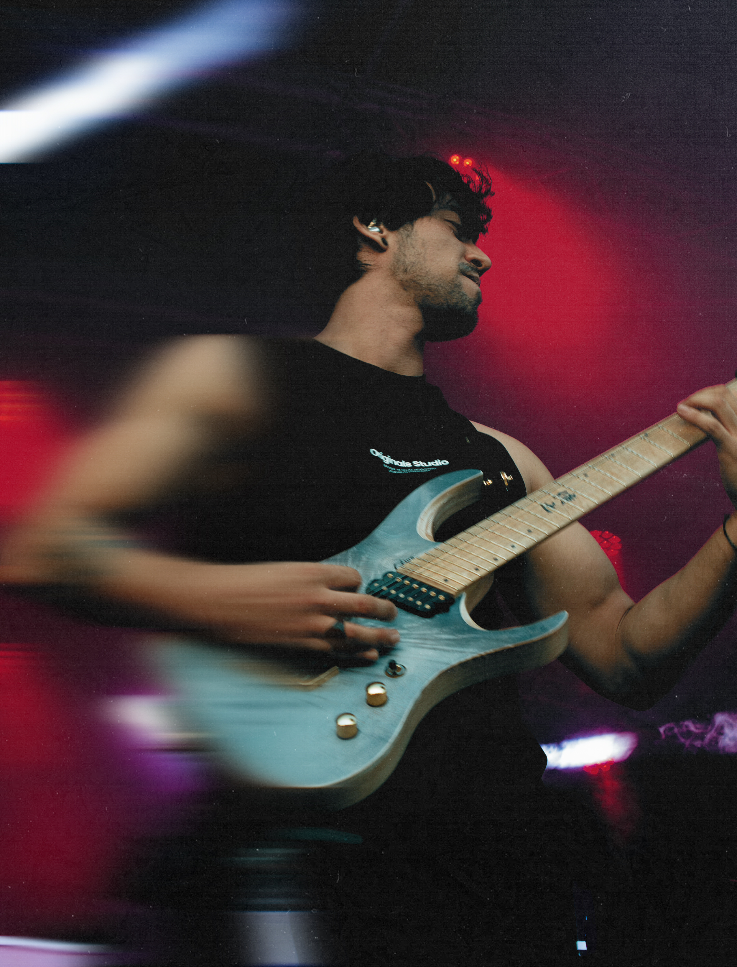 A man playing an electric guitar on stage with colorful lights and motion blur effects.