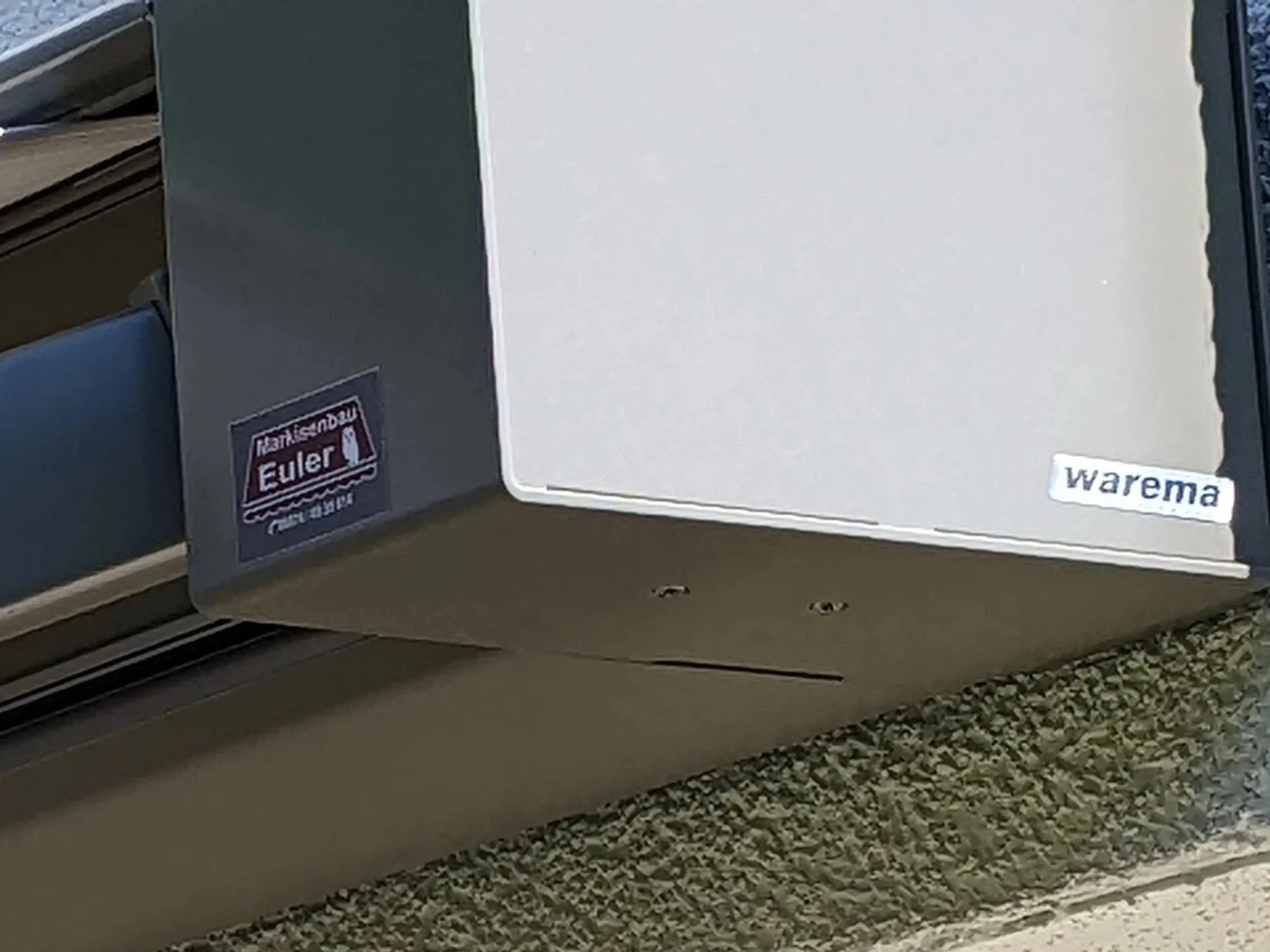 Der Kühlschrank steht vor einer grauen Wand im Laden, ist dunkelgrau und hat einen Aufkleber mit dem Text "Euler" und eine Eishockey-Mütze. Auf der rechten unteren Ecke des Kühlschranks befindet sich ein Aufkleber mit dem Text "warema".