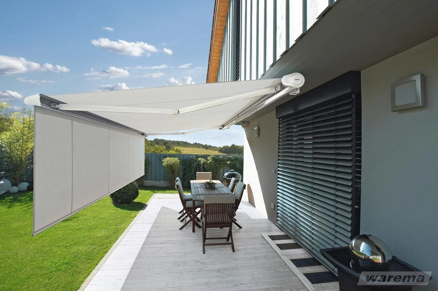 Blick auf eine Terrasse mit einem Essbereich, einem Sonnenschutzschirm, einem Sonnenschutz, Garten und Himmel