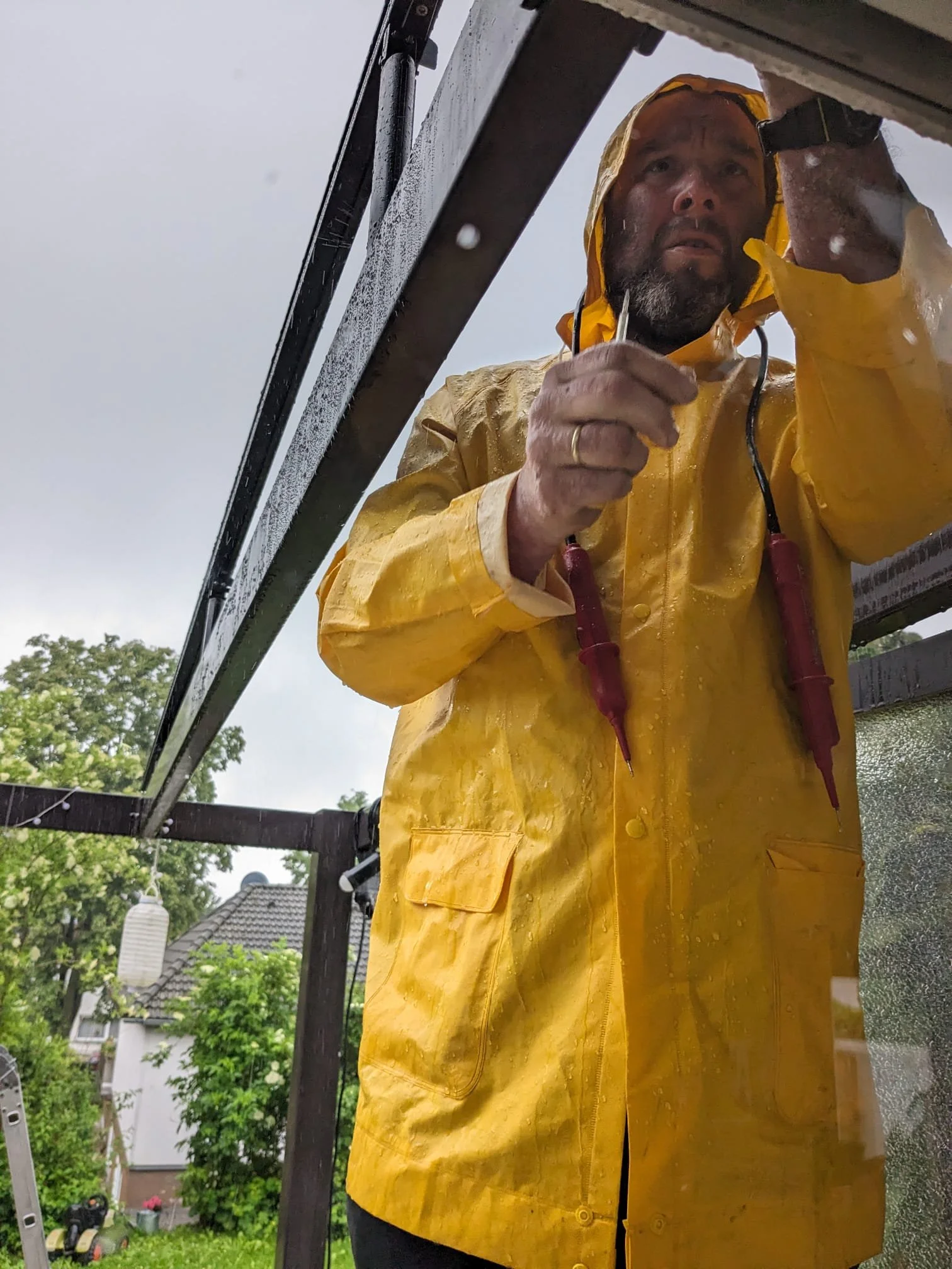 Mann in gelber Regenjacke, der draußen an einer Leiter arbeitet und ein Multimeter benutzt.